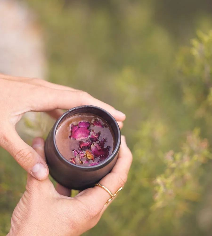 A hand holding a cup of ceremonial cacao outdoors