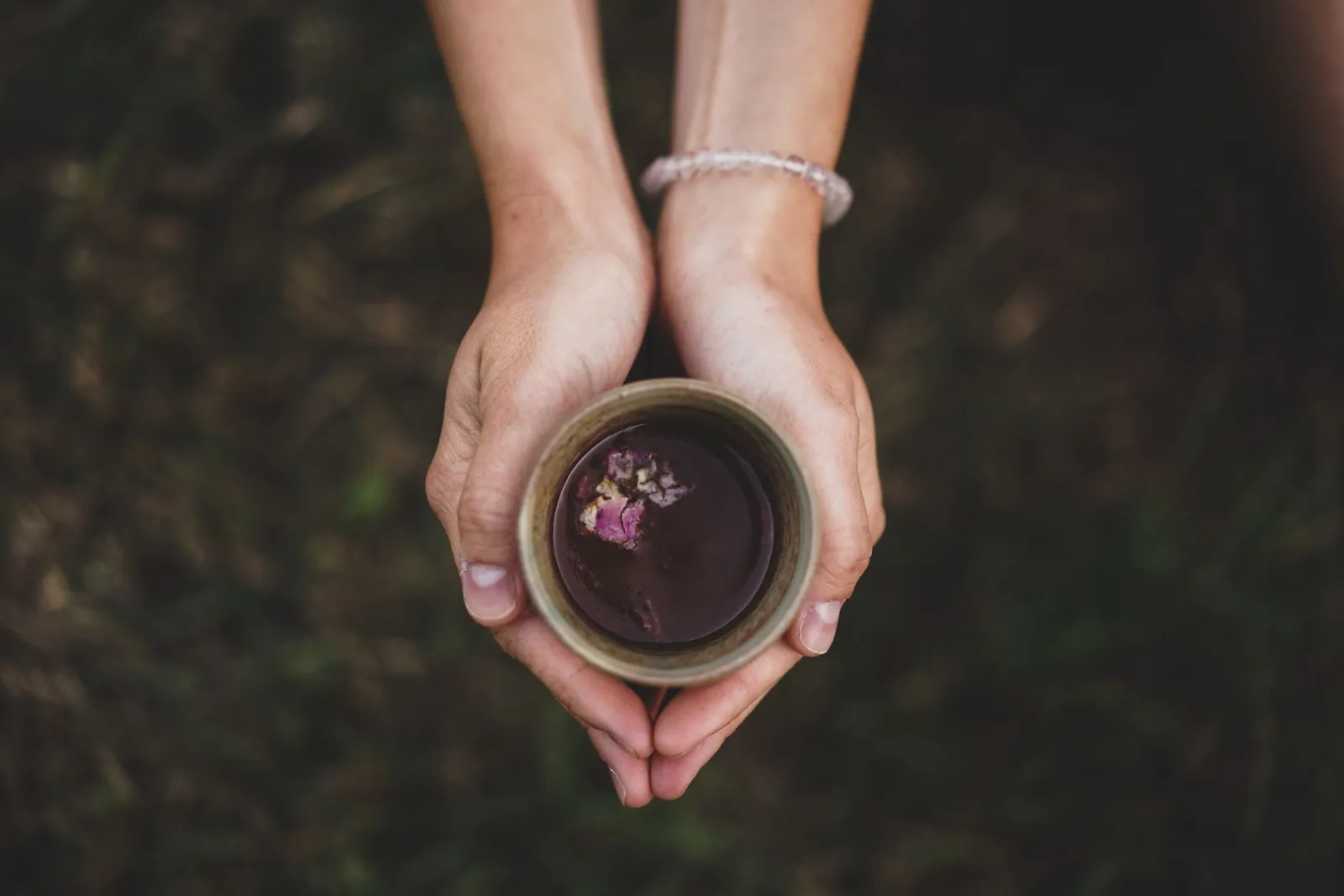 Two hands holding a cup of Ceremonial Cacao with rose petals